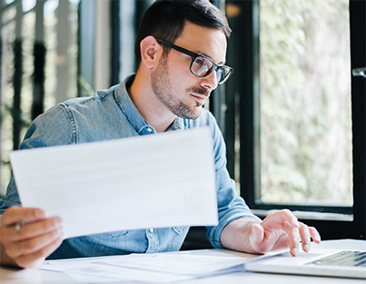 Homem utilizando um notebook enquanto segura uma folha de papel