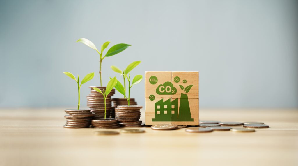 Mudas brotando em pilhas de moedas ao lado de bloco com ícone de fábrica e CO₂, simbolizando finanças sustentáveis.