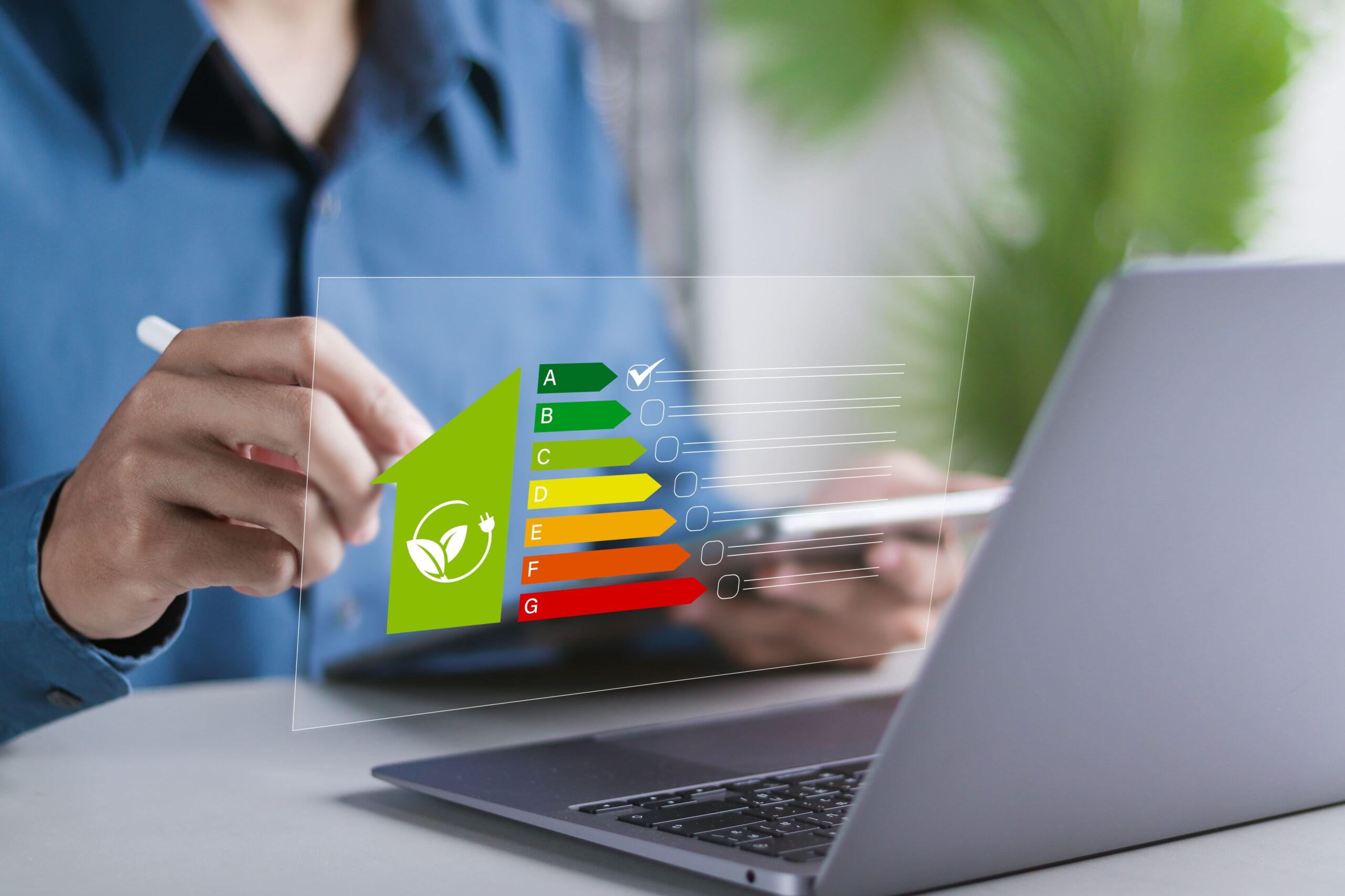 Pessoa usando laptop e celular com etiqueta de eficiência energética (A–G) em destaque na tela.